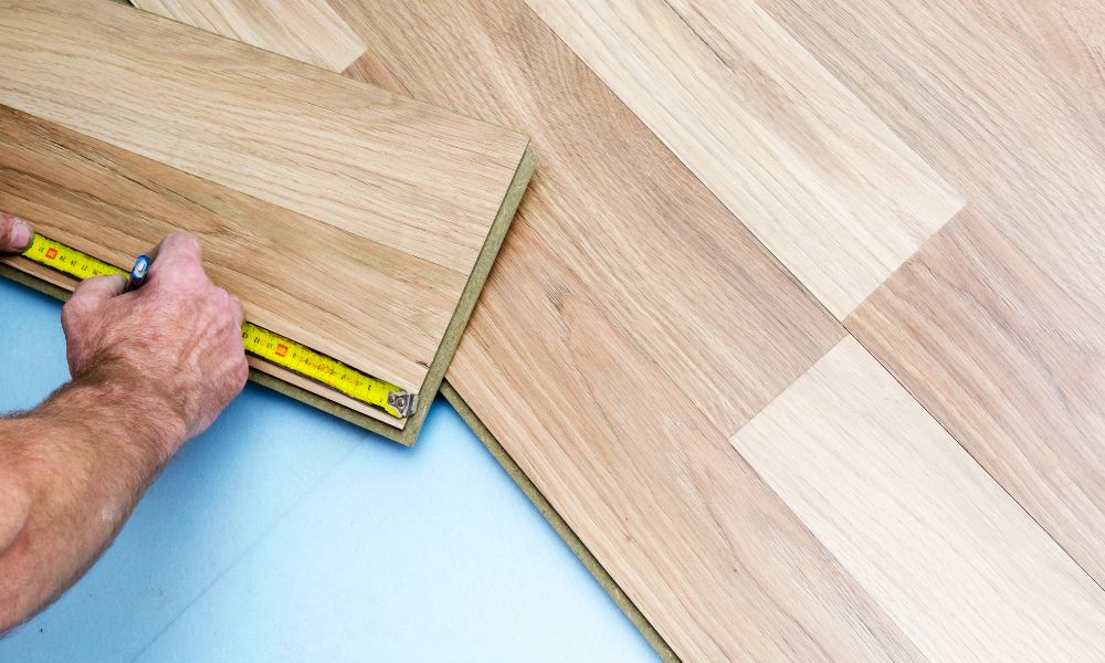 An image of a person measuring and installing wood flooring.